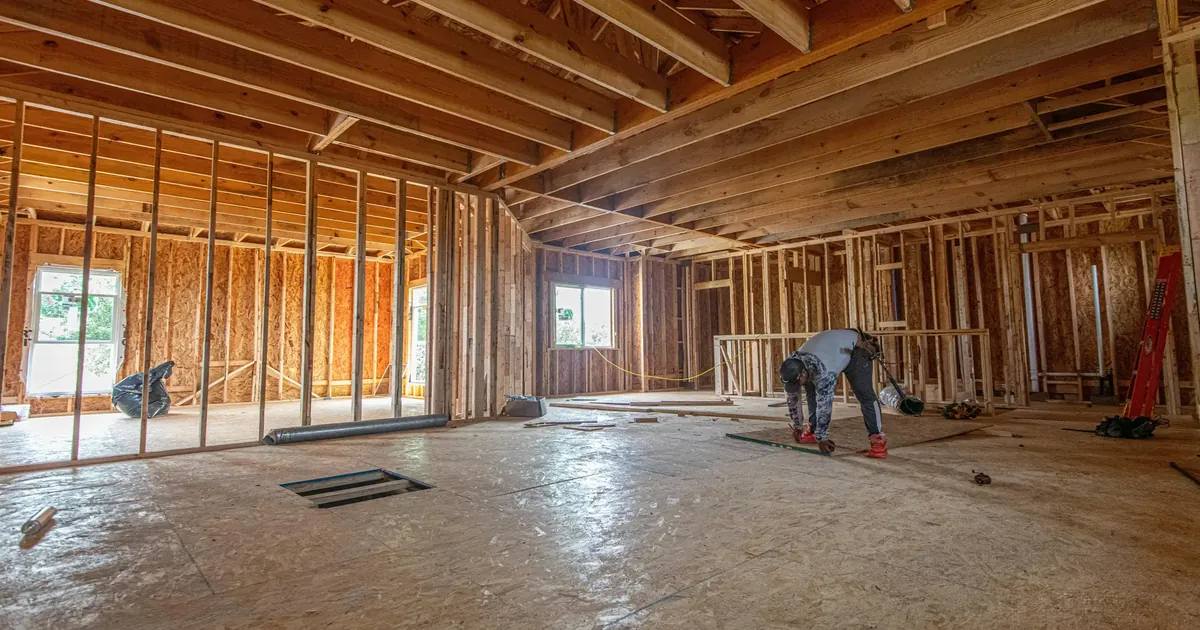 Carpenter working inside a wood-framed building with exposed wall studs and roof trusses